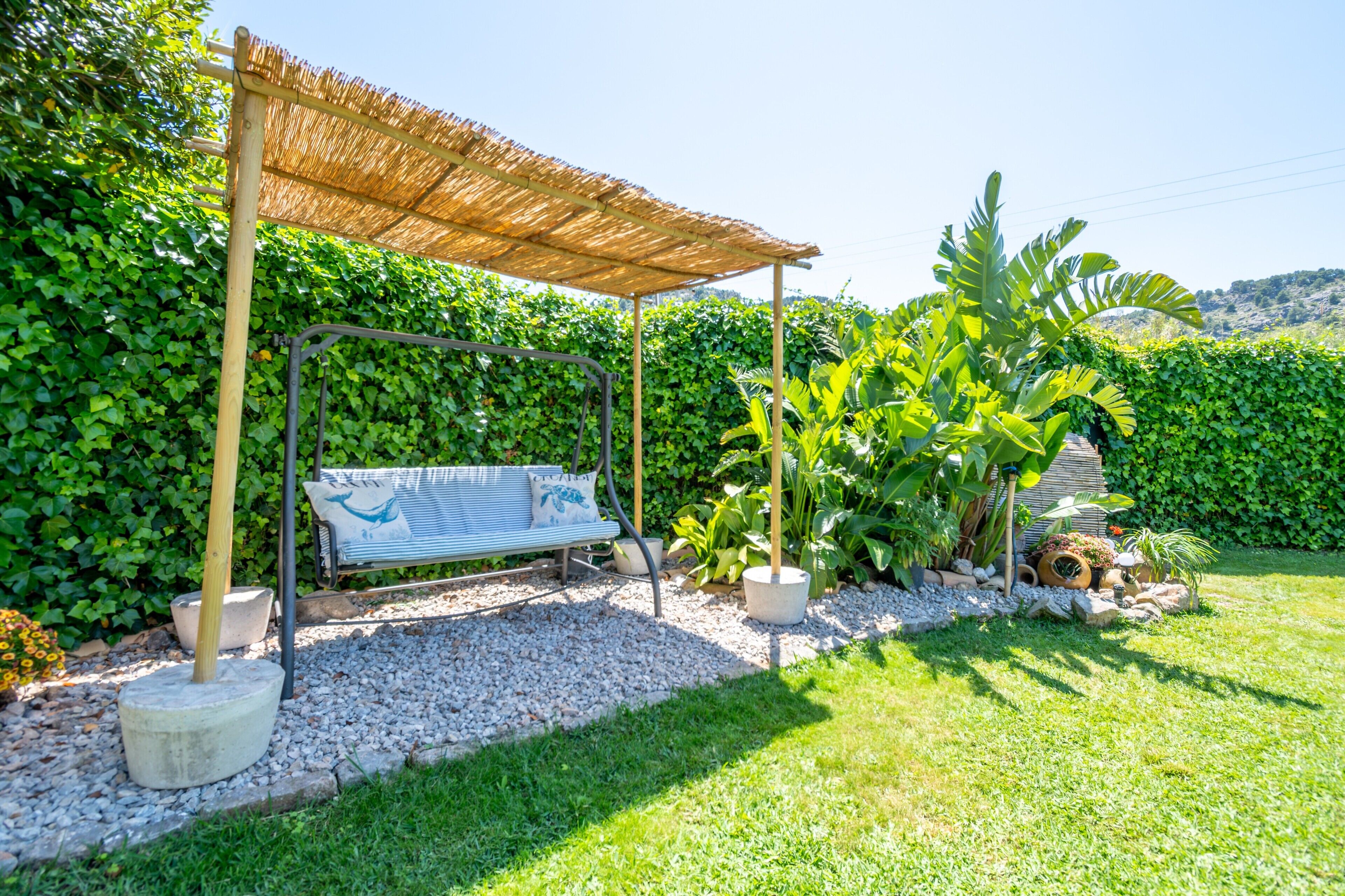 Un jardín con una mecedora, un banco y una estructura cubierta de paja.