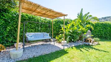 Un jardín con una mecedora, un banco y una estructura cubierta de paja.