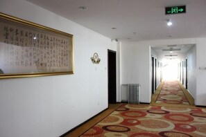 Un pasillo de hotel con piso alfombrado, una obra enmarcada en la pared y una señal de salida.