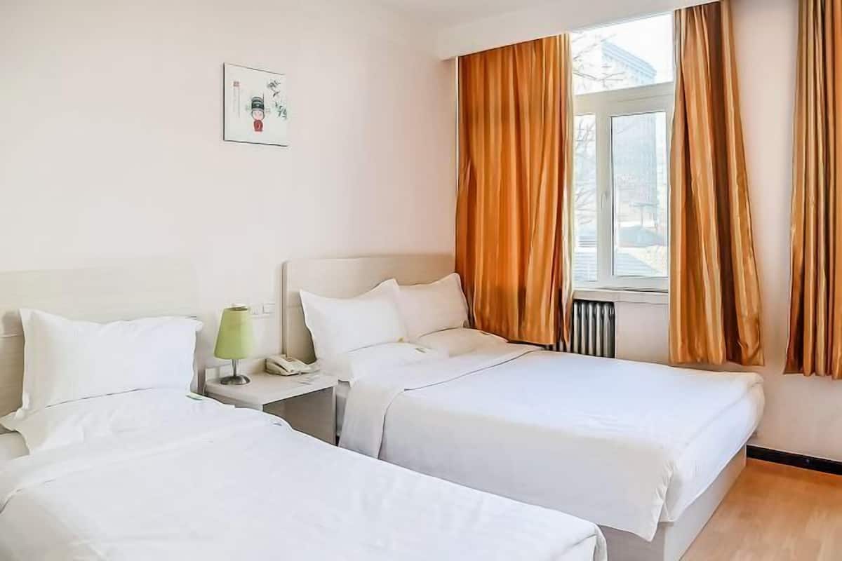 Ein Hotelzimmer mit zwei Betten, einem Nachttisch mit Lampe, einem Fenster mit Vorhängen und einem Heizkörper.