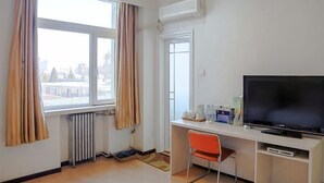 Ein Hotelzimmer mit großem Fenster, einem Schreibtisch mit Fernseher und einer Heizung.