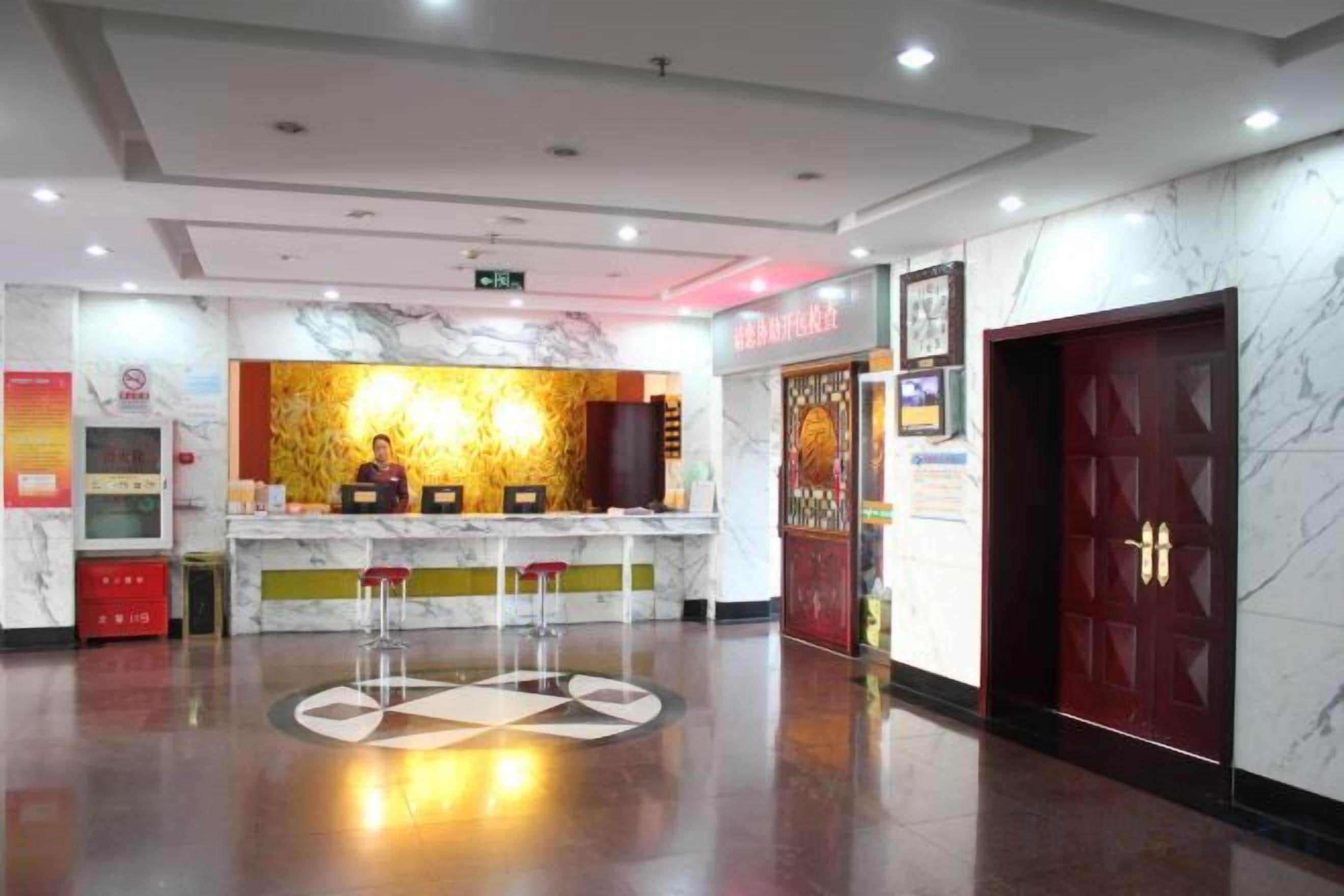 Un espace d’accueil d’hôtel avec un comptoir en marbre, deux tabourets de bar, une porte rouge et un mur en marbre.