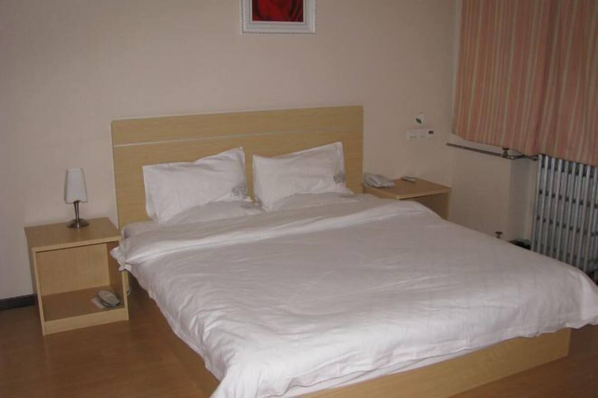 Ein ordentlich bezogenes Bett mit weißer Bettwäsche, ein Nachttisch mit Lampe und ein an der Wand befestigtes Telefon.
