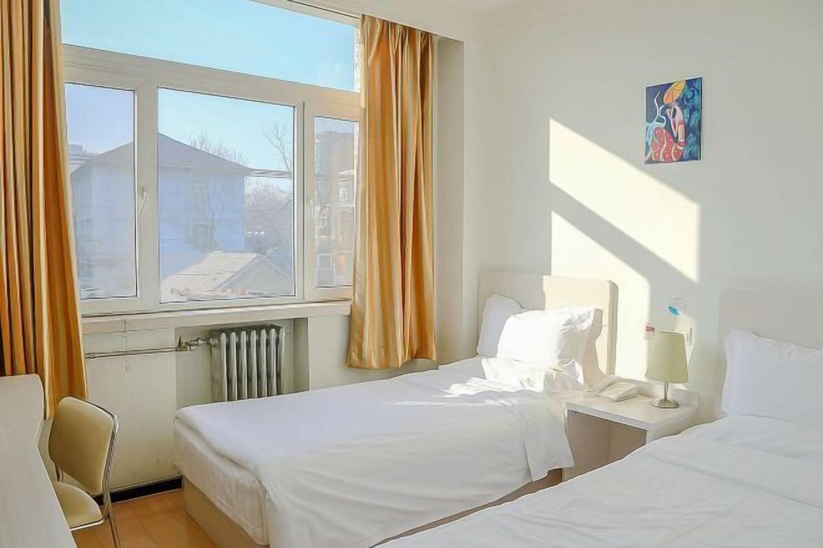 Ein Hotelzimmer mit zwei Betten, einem Sessel, einem Heizkörper und einem fenster mit Vorhängen.