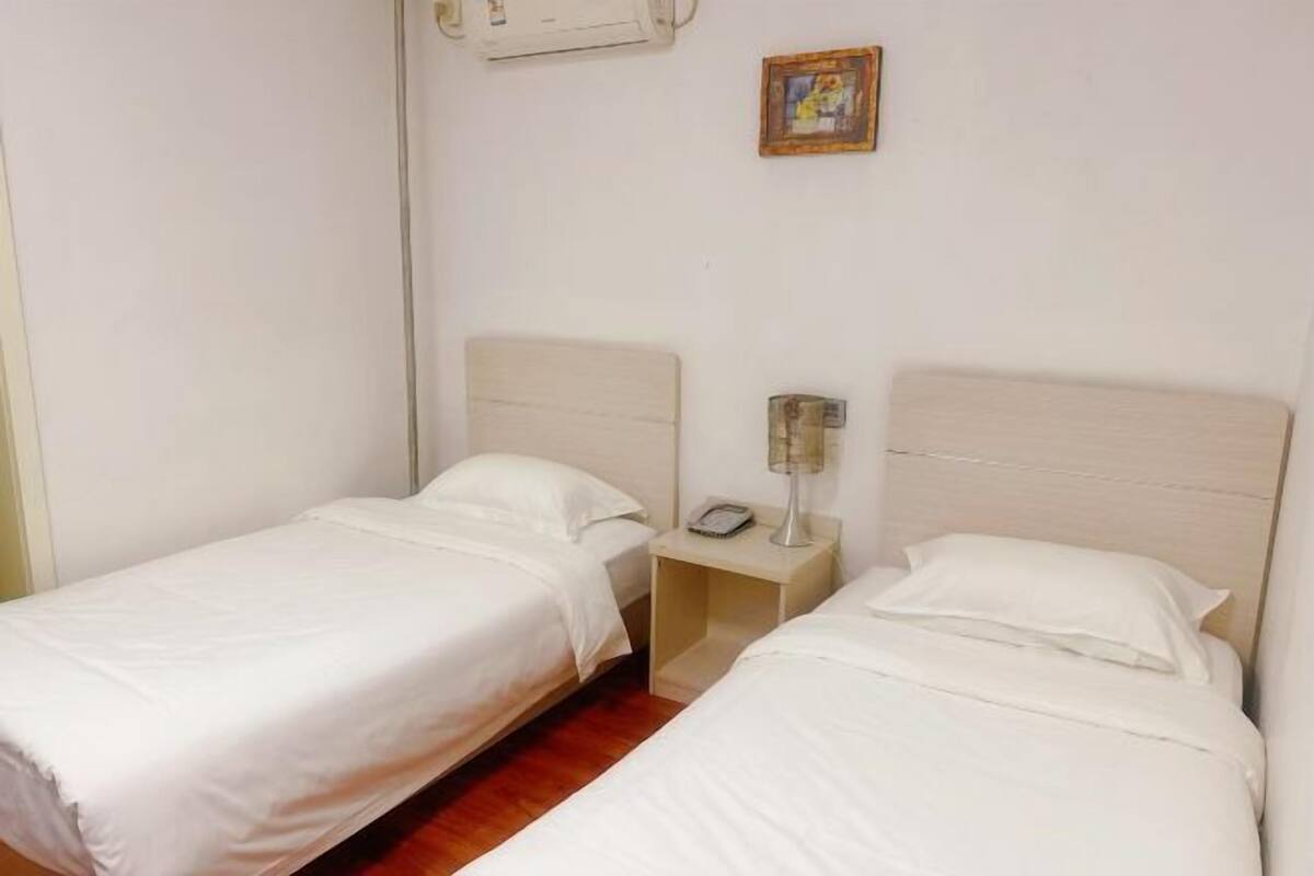 Ein Hotelzimmer mit zwei Einzelbetten, einem Nachttisch mit Lampe, einem Telefon und einem Bild an der Wand.