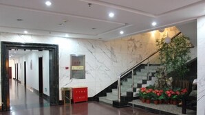 Eine Hotelhalle mit einer Marmortreppe, einem roten Schrank und Topfpflanzen.