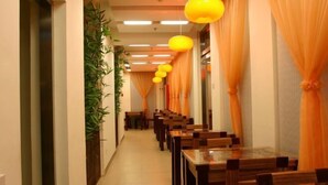 Ein Korridor mit Tischen und Stühlen, orangefarbenen Vorhängen und hängenden gelben Lampen.