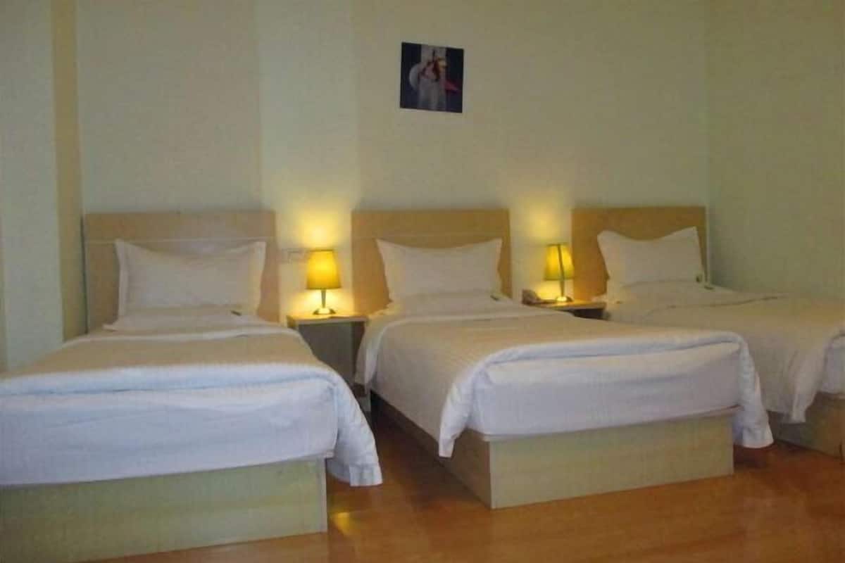 Ein Hotelzimmer mit drei Einzelbetten, jeweils mit Nachttisch und Lampe.