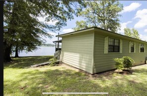 Situated by a body of water, this cabin features a front porch and a small enclosed area.