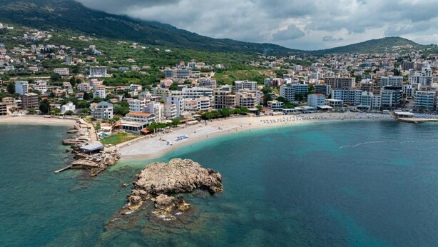 An aerial view of a coastal city with a beach, rocky outcrops, and dense urban development. - Elma Hotel (Bar)