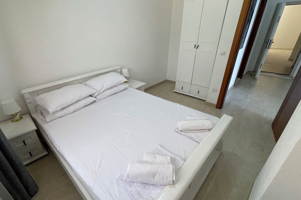 Un lit bien fait, avec du linge de lit blanc, une table de chevet avec une lampe et une armoire à deux portes.