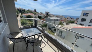 A balcony with a table and chairs, overlooking a coastal town with buildings and the sea. - Elma Hotel (Bar)