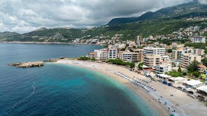 Uma cidade costeira com praia, edifícios e montanhas ao fundo.