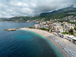Un pueblo costero con una playa, edificios y montañas al fondo.