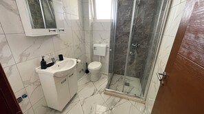 A bathroom with a white sink, toilet, and glass shower enclosure. - Elma Hotel (Bar)