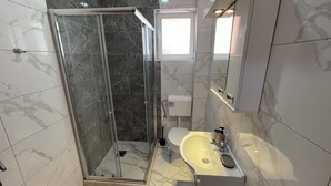 A bathroom with a glass-enclosed shower, a toilet, and a sink.