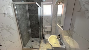 Un baño con ducha de mampara de vidrio, inodoro y lavamanos.