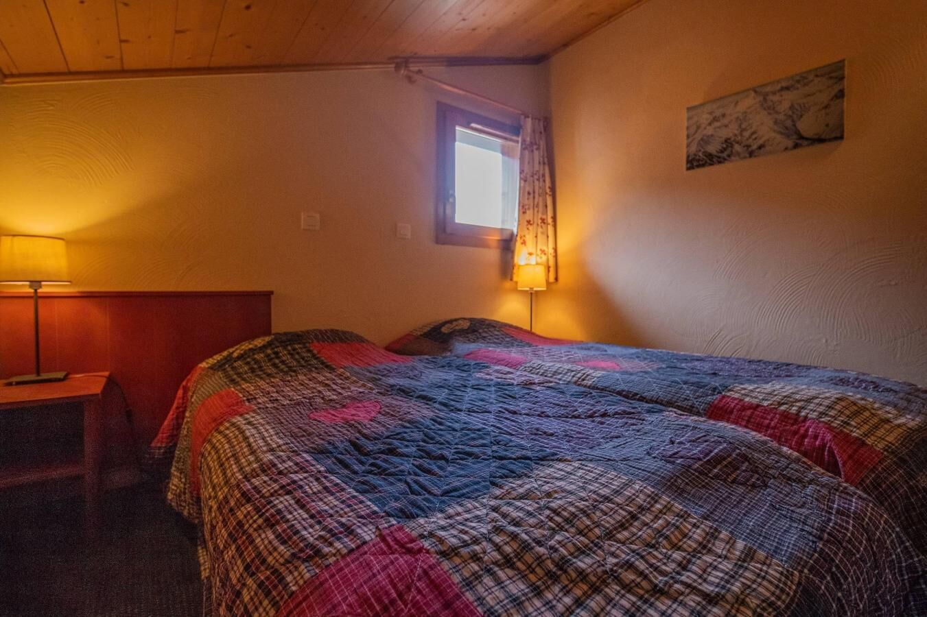 A room with a bed, a nightstand, a lamp, a window, and a painting on the wall.