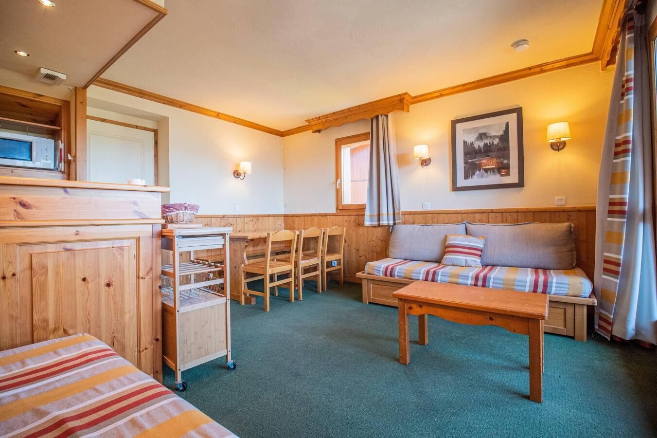 A cozy room with a wooden sofa, a dining table, and a kitchen area with a microwave.