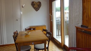 Un coin repas avec une table et des chaises en bois, un élément de décoration murale en forme de cœur et une vue dégagée grâce à de grandes portes-fenêtres coulissantes.