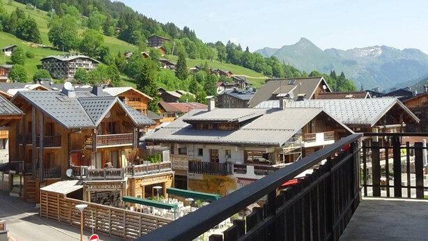 Un village de montagne aux maisons en bois, doté de balcons et offrant une vue sur les collines et les montagnes environnantes.