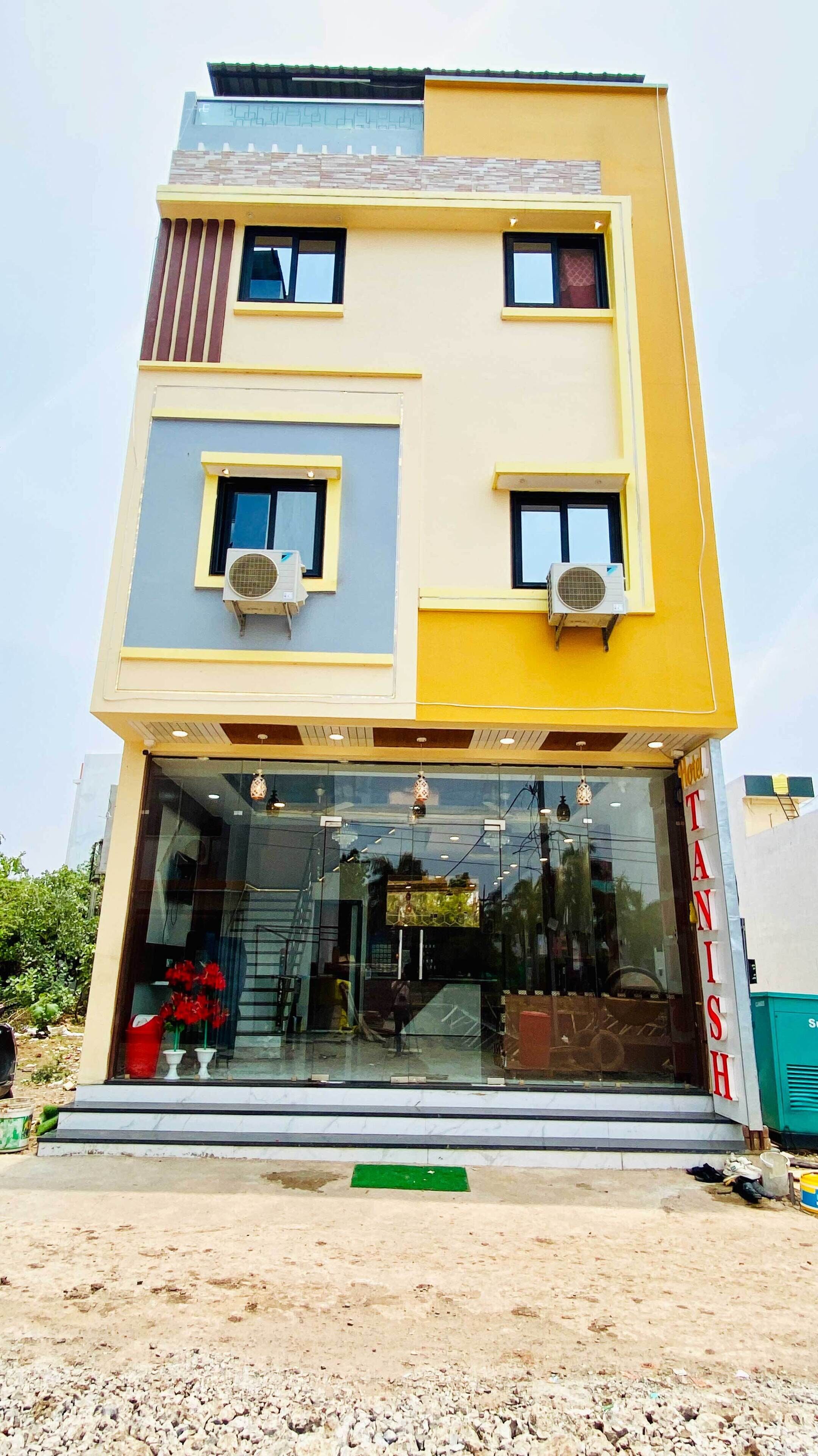 A two-story building with a yellow and grey facade, large windows, and air conditioning units.