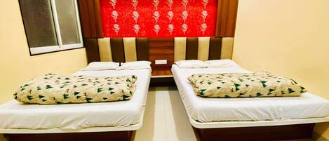 A hotel room with two single beds, each with a white mattress and a patterned pillow. The headboard is wooden with a red decorative panel.