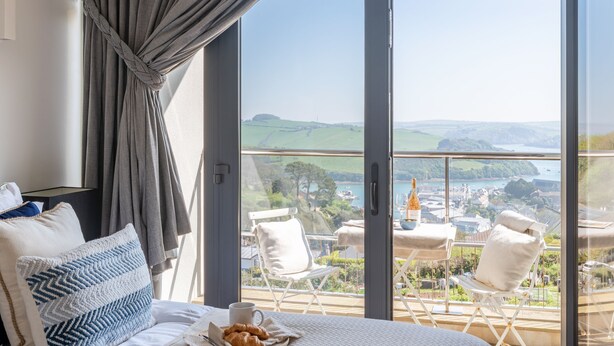 Een slaapkamer met een groot raam dat uitkijkt op een prachtig uitzicht over heuvels en een wateroppervlak.