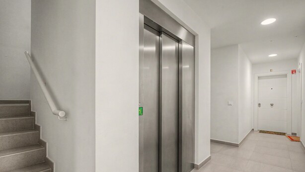 Un corridoio con una scala, una porta contrassegnata da un numero e un rilevatore di fumo.