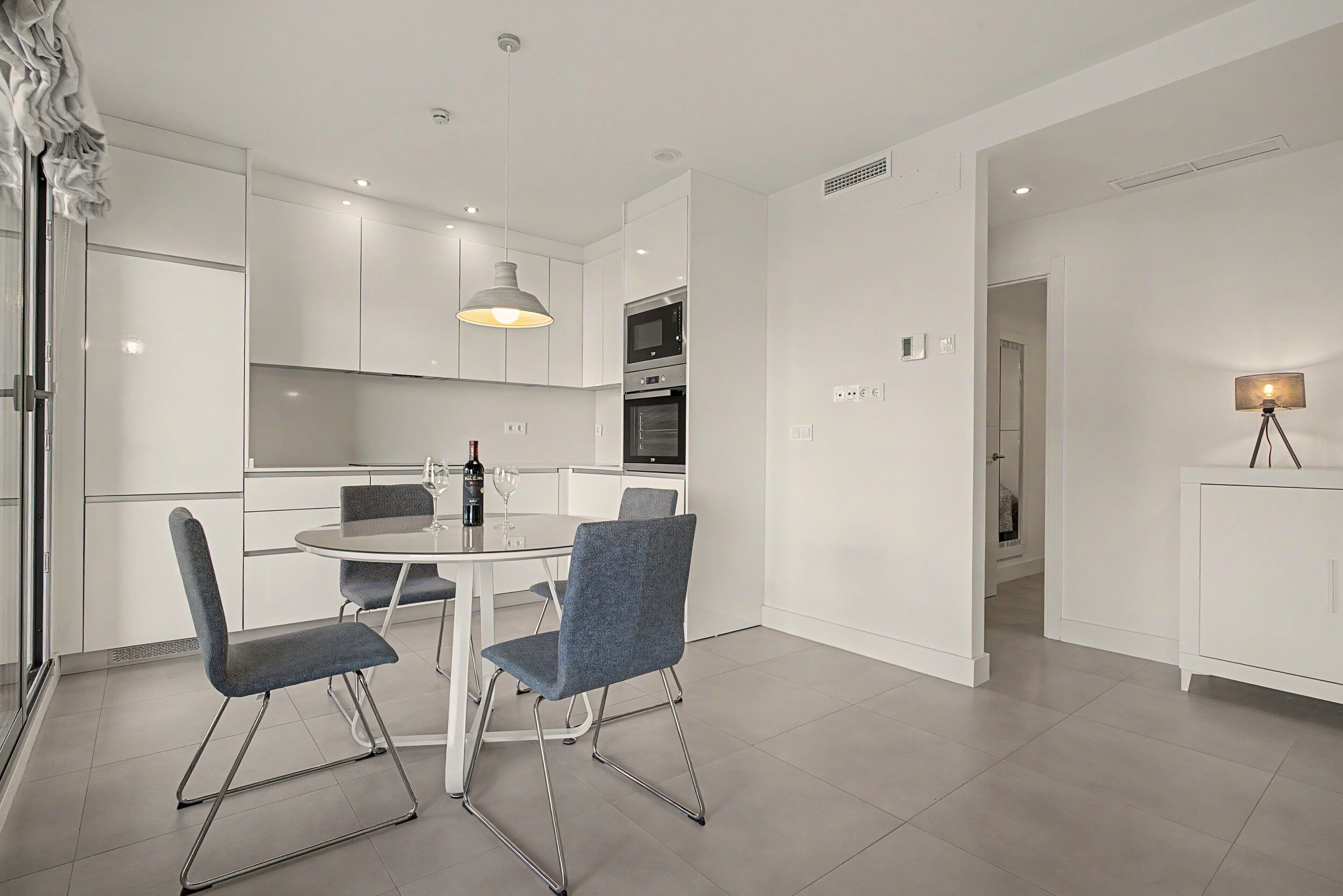 Een moderne keuken met witte kastjes, een eettafel met stoelen en een hanglamp.