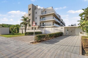 A modern multi-story residential building with balconies, a pedestrian crossing sign, and a gated entrance.
