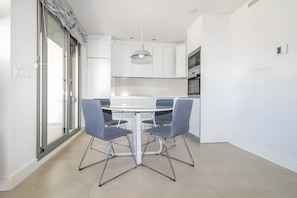 Une cuisine moderne avec des meubles blancs, un îlot central et un coin repas comprenant une table ronde et des chaises.