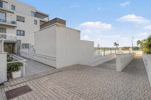 Een modern gebouw met een plat dak, een glazen balkon en een verhard voetpad.