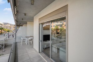 Een balkon met een glazen deur, witte stoelen, een klein tafeltje en een flatscreen televisie.