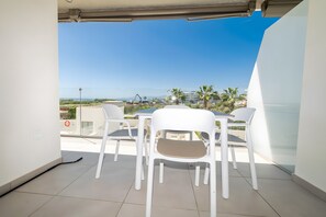 Een balkon met een tafel en stoelen, met uitzicht op een kustgebied met gebouwen en palmbomen.