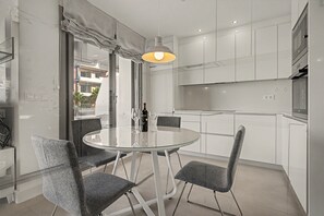 A modern kitchen with white cabinets, a glass dining table, and grey chairs.