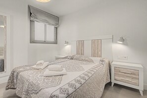A bedroom with a bed, a nightstand, a lamp, a window with a curtain, and a wall-mounted light fixture.