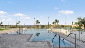 Una piscina con bordo piastrellato, circondata da palme e un cielo sereno.