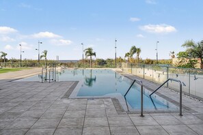 A swimming pool with a tiled deck, surrounded by palm trees and a clear sky.