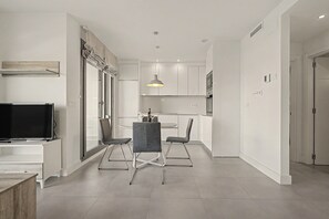 Een moderne keuken met witte kasten, een eethoek met twee stoelen, een televisie en een hanglamp.