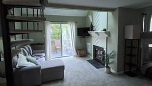 Un salon avec un canapé, une cheminée, un téléviseur et un escalier.