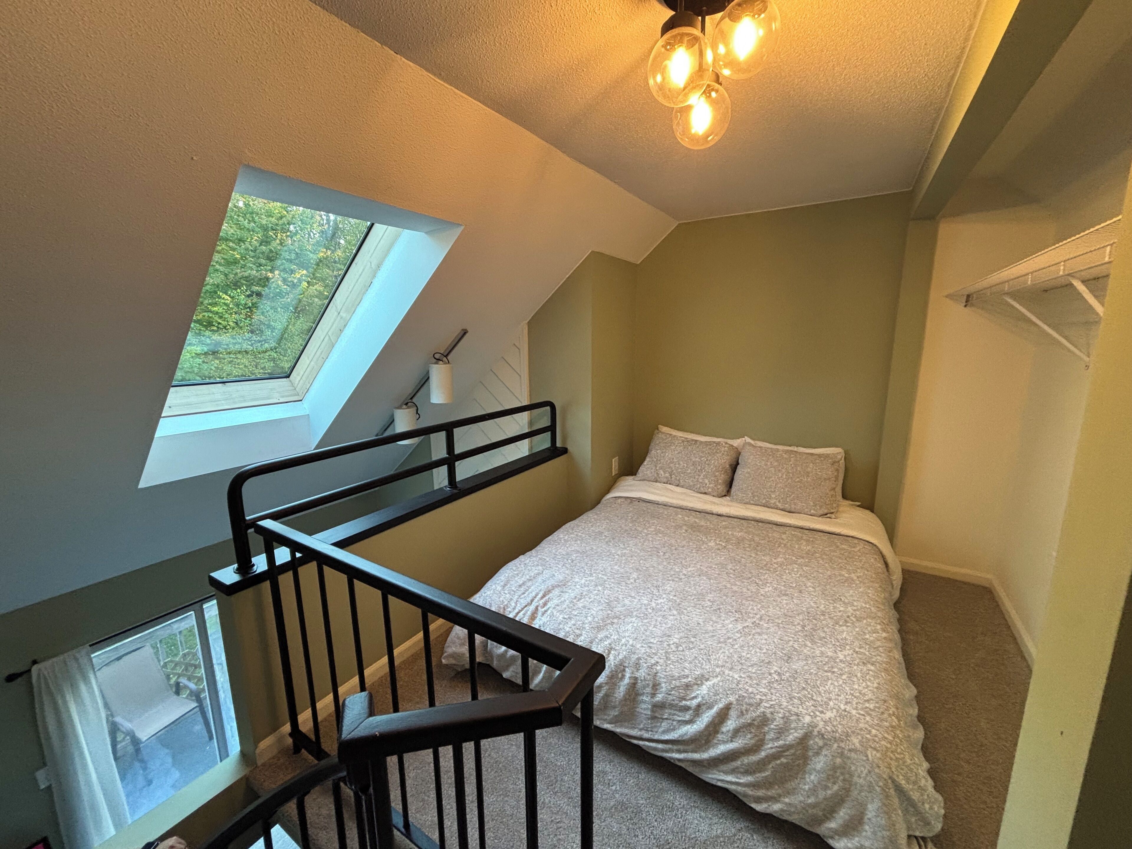 Een slaapkamer met dakraam, een bed, een trap en een plafondlamp.