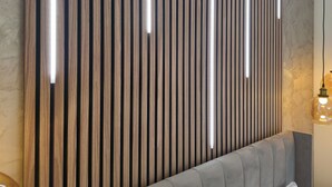 A modern room with a grey upholstered headboard, a wooden slat wall with integrated lighting, and a marble-like textured wall.