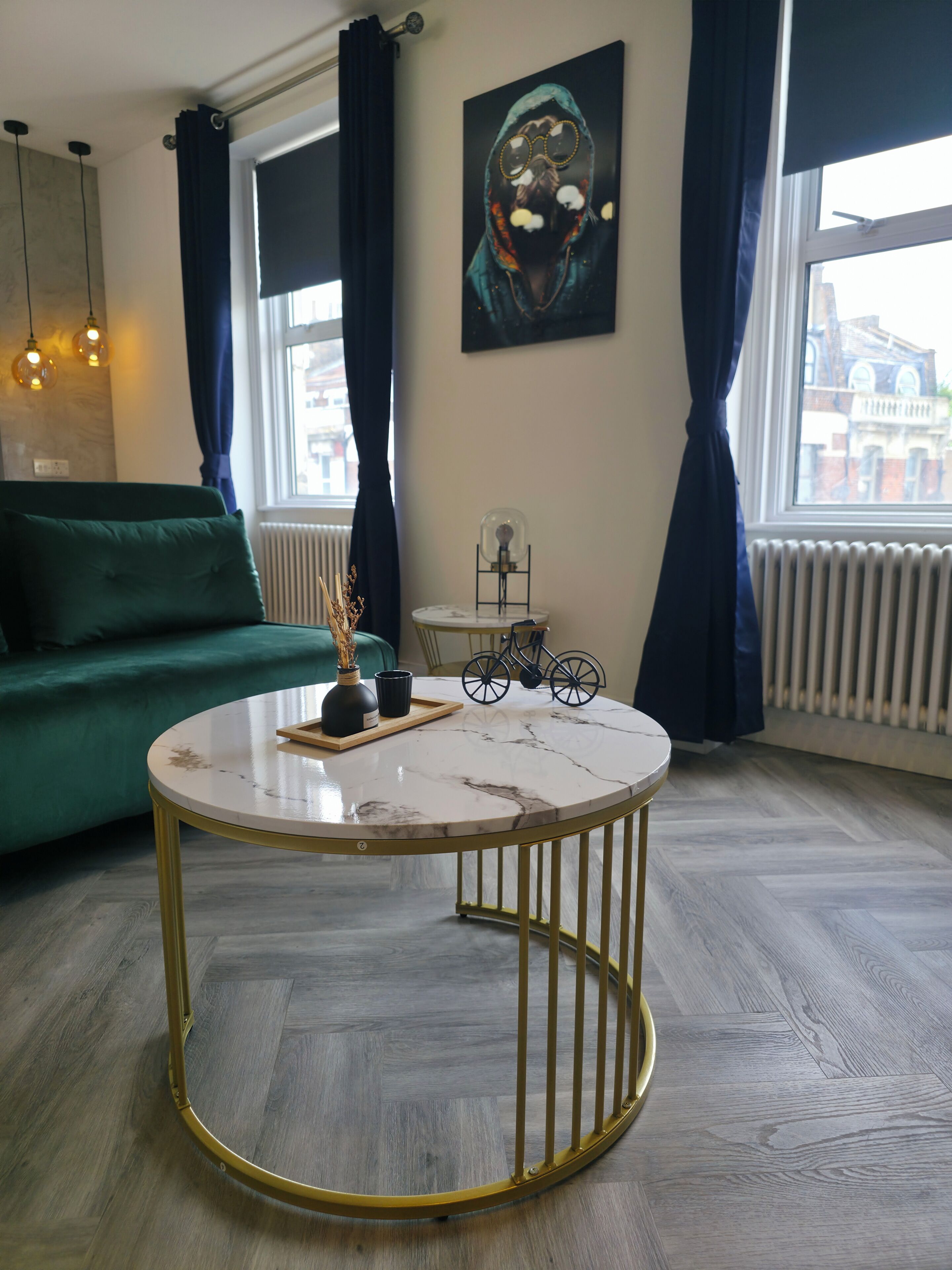 A modern living room with a round marble coffee table, a green sofa, and a bicycle decoration on a small table.