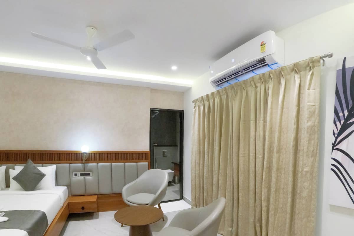 A modern hotel room with a bed, two chairs, a small table, an air conditioning unit, and a curtain.