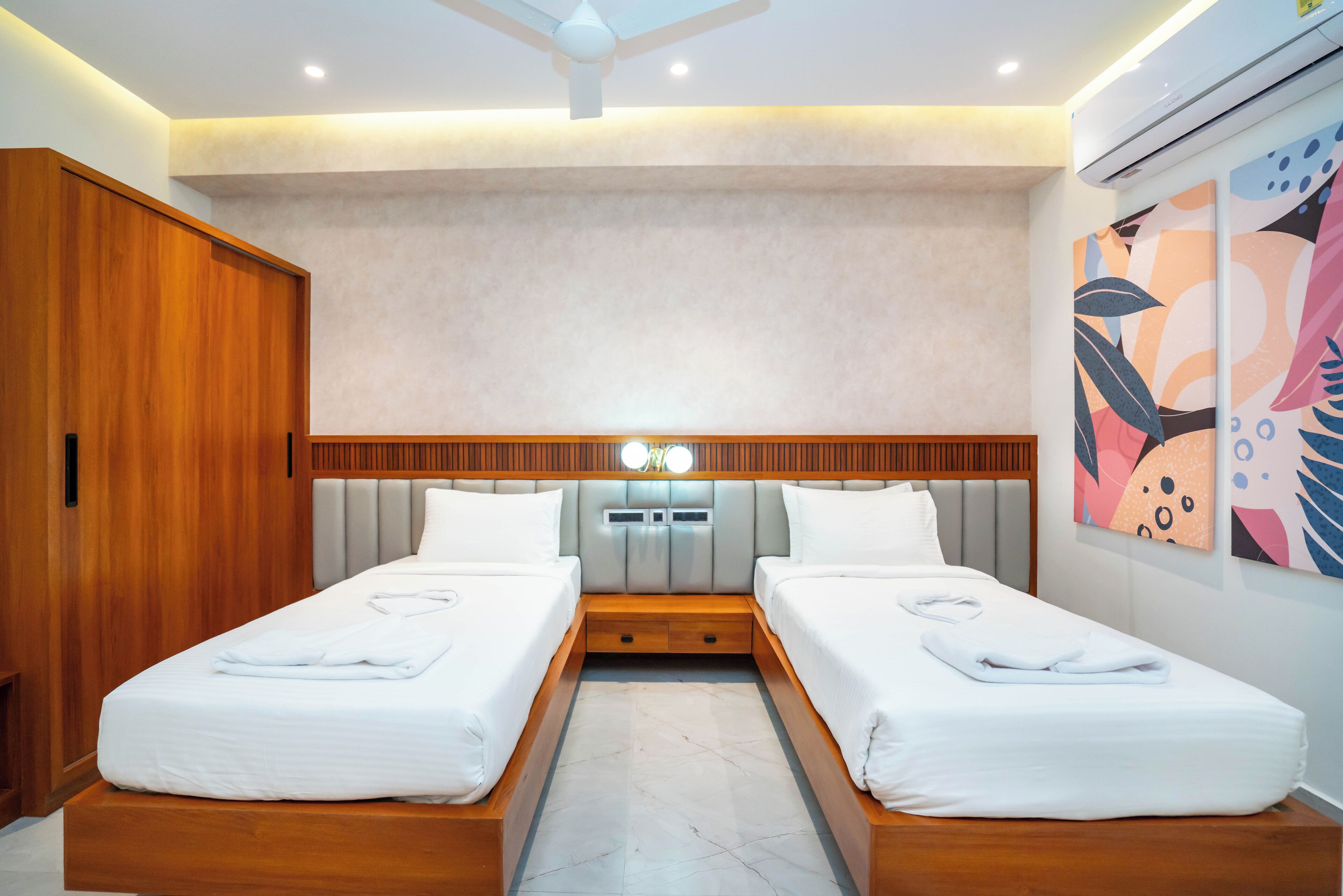 A hotel room with two single beds, a wooden wardrobe, a ceiling fan, and a wall-mounted air conditioner.