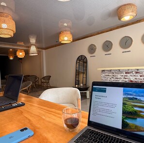 Una habitación con una mesa de madera, dos computadoras portátiles, una copa de vino y una computadora portátil mostrando una página web. Hay lámparas de mimbre, un espejo y relojes en la pared.