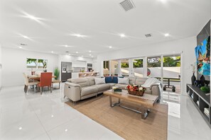 A spacious living room with a large sofa, a coffee table, and a dining area with chairs and a table. - Family Retreat: Pool, Games & Private Apartment (Miami)