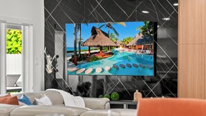 A modern living room with a large flat-screen TV mounted on a black wall, a sofa, and a coffee table. - Family Retreat: Pool, Games & Private Apartment (Miami)