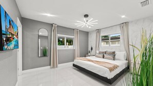 A modern bedroom with a large bed, a ceiling light fixture, a window, and a wall-mounted TV. - Family Retreat: Pool, Games & Private Apartment (Miami)